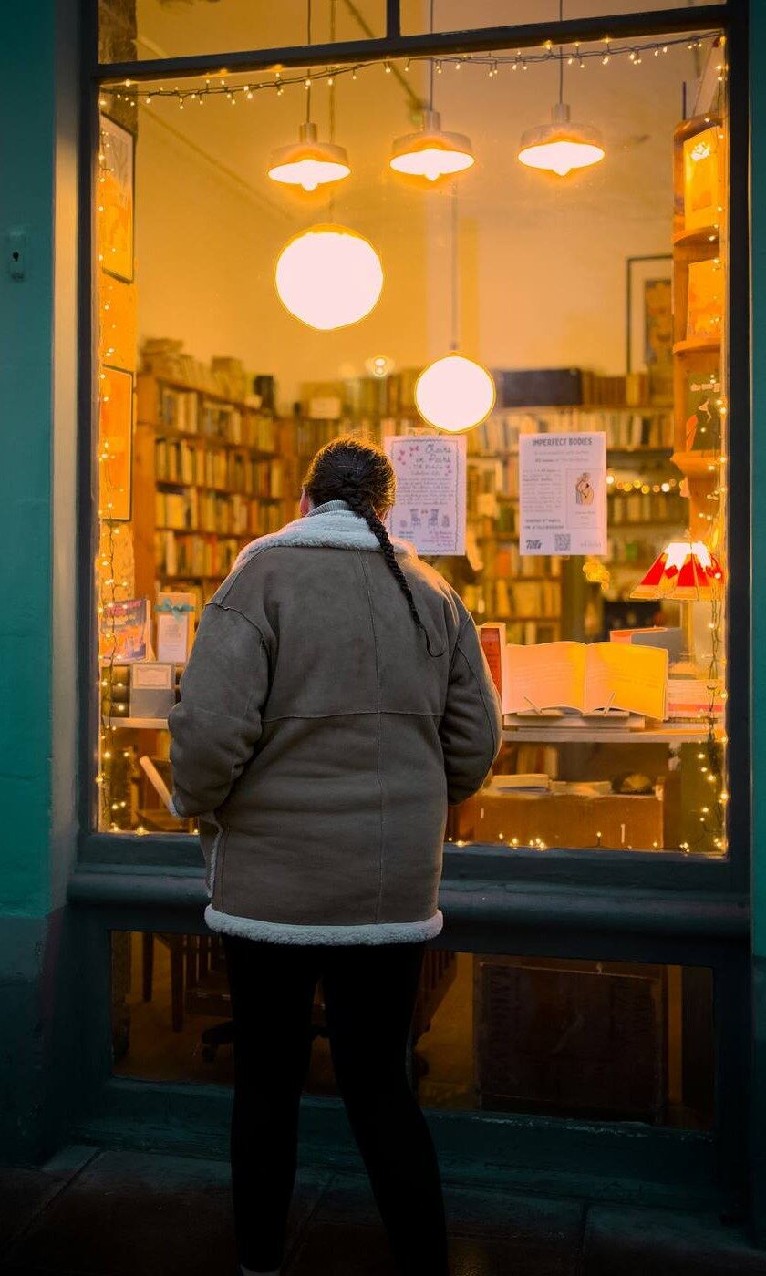 Una lectora mirando un escaparate de librería iluminado, de noche